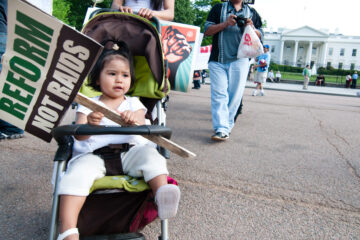 Toddler holding immigration protest sign sitting in stroller